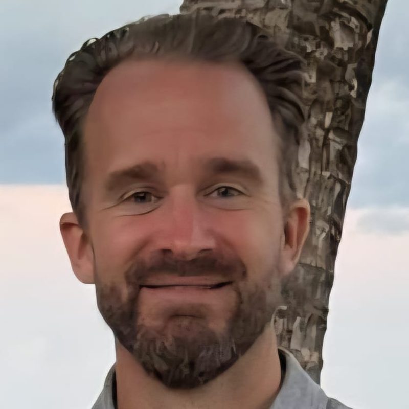 Simo D smiling on a beach in Belize, with a palm tree and the Caribbean Sea behind him